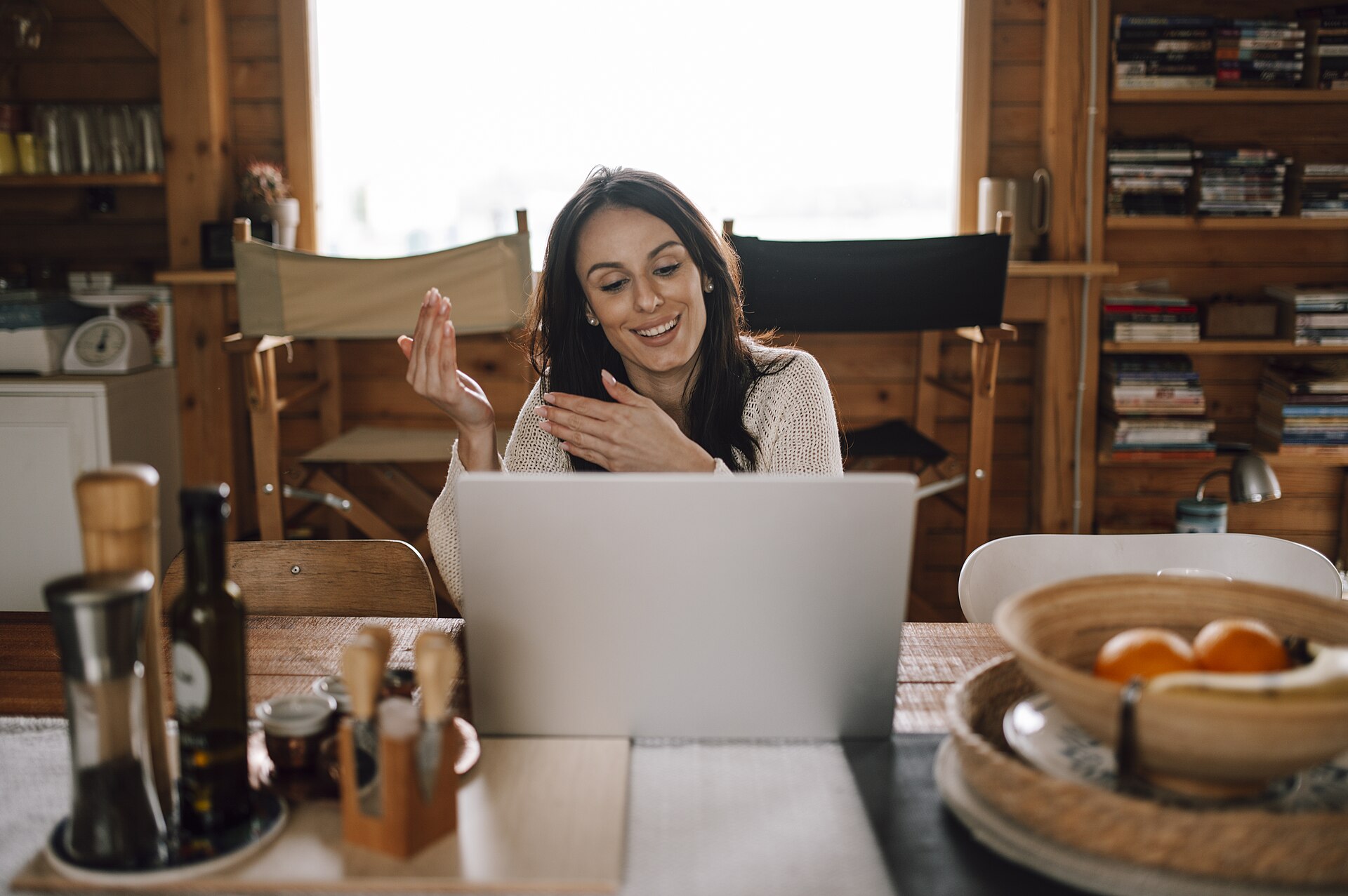 Woman smiling and using laptop during video call in cozy wooden room